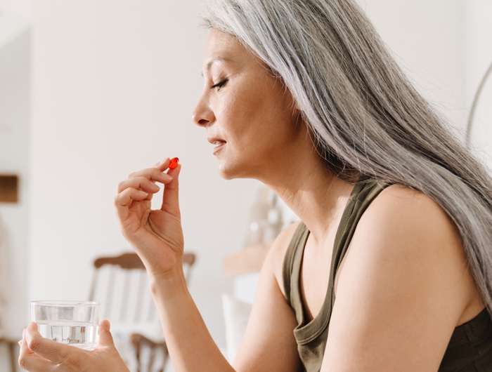woman holding a glass of water and red supplement close to her mouth